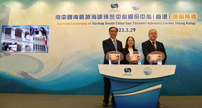 Three individuals are participating in the opening ceremony of the Backup South China Sea Tsunami Advisory Center in Hong Kong, standing behind a podium with their hands on illuminated buttons.